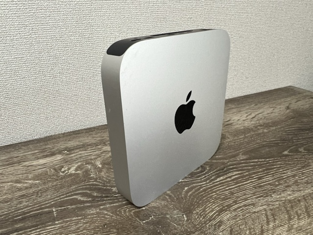 木目調のデスクに縦置きされたMac mini（M1チップ搭載）のシルバー本体